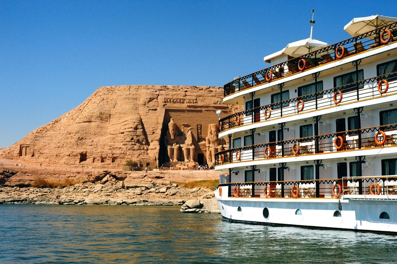 "Cruise ship sailing along the Nile River with the ancient Abu Simbel Temple in the background under a clear blue sky